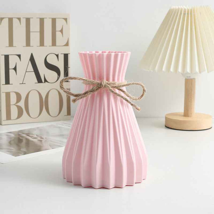 Nordic durable plastic flower vase in pink with twine bow, displayed with decorative items on a modern table.